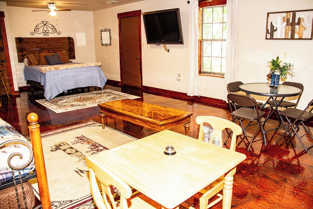 A room with a bed, a television, a dining table with chairs, and a window with curtains.