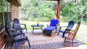 Een overdekt terras met vier Adirondack-stoelen, een loungestoel met blauwe kussens, een bijzettafeltje met een vaas en een schommelstoel.