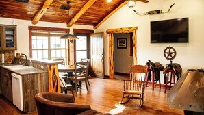 Een rustiek interieur met houten balken, een eethoek, een keuken met spoelbak en een aan de muur bevestigde televisie.