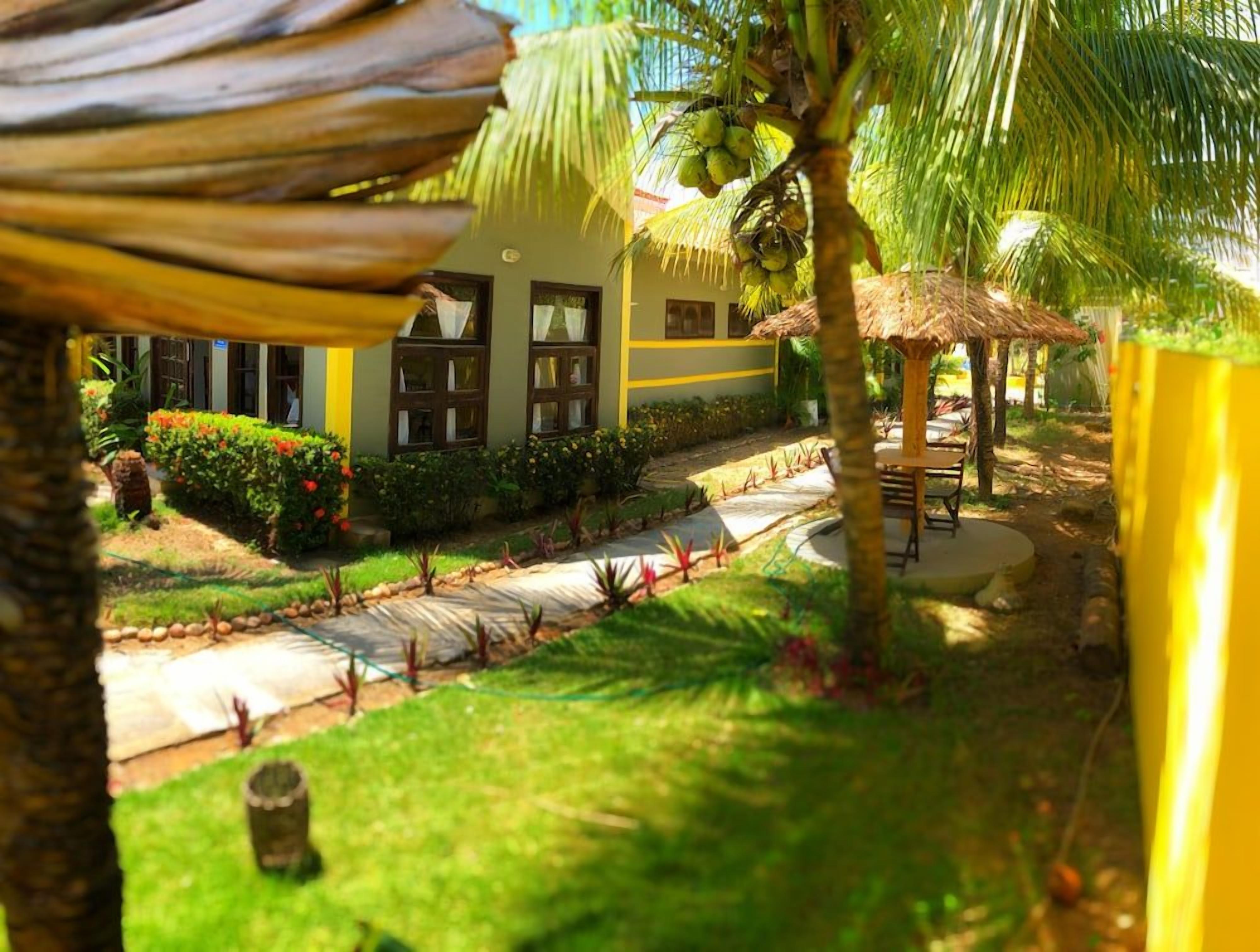 Um resort tropical com um gazebo de palha, palmeiras e um jardim bem cuidado.
