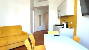 A compact living space with a sofa, a dining table, chairs, a kitchen area, and a TV mounted on the wall. - Colori di Trieste - TriesteCenter (Trieste)