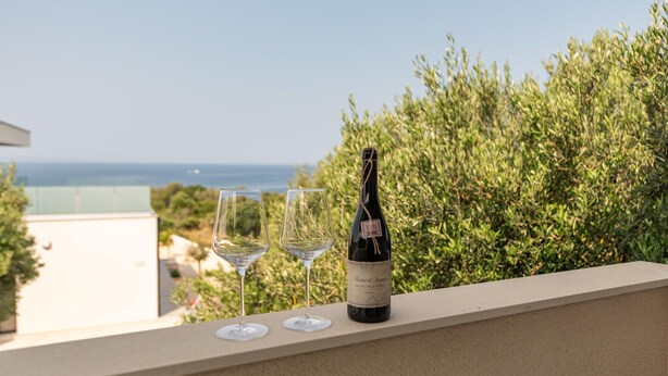 Een balkon met een fles wijn en twee glazen, met uitzicht op de kust.