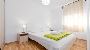 Een nette, moderne hotelkamer met een groot bed, twee nachtkastjes met lampen, een houten vloer en een raam met dunne gordijnen.