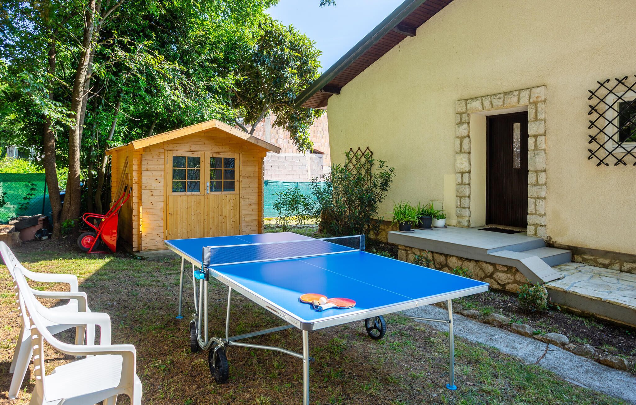 An outdoor ping pong table set up in a backyard with a wooden shed and a house in the background.
