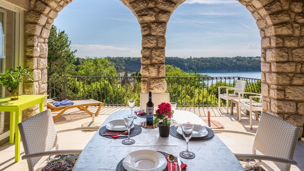A dining area with a table set for two, overlooking a scenic view of a lake and forest. - One bedroom beautiful home in Omisalj (Omisalj)