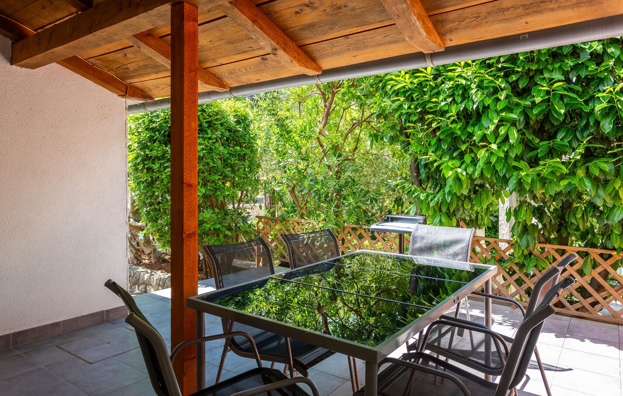 Eine Terrassengruppe im Freien mit Glastisch und Metallstühlen, umgeben von üppiger Bepflanzung und einer Holz-Pergola.