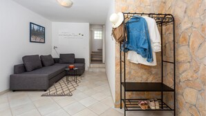 A modern living room with a grey sofa, a small table with a lamp, a stone wall, and a metal rack with clothes and shoes.