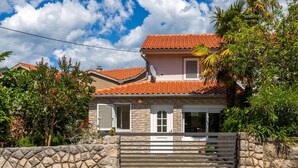 A two-story house with a stone facade, a red-tiled roof, and a gated entrance.