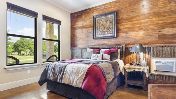 Un dormitorio con una cama grande, paredes de madera, un ventanal con vistas y una mesita de noche con lámpara.
