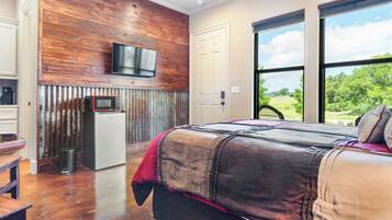 A bedroom with a large bed, a television mounted on a wooden wall, and a view of the outdoors through a large window.