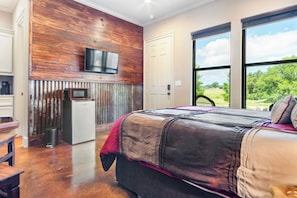 Une chambre avec un grand lit, un téléviseur fixé au mur en bois, et une vue sur l’extérieur grâce à une grande fenêtre.