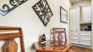 Un comedor con una mesa y sillas de madera, un adorno en la pared y un mueble con cafetera.