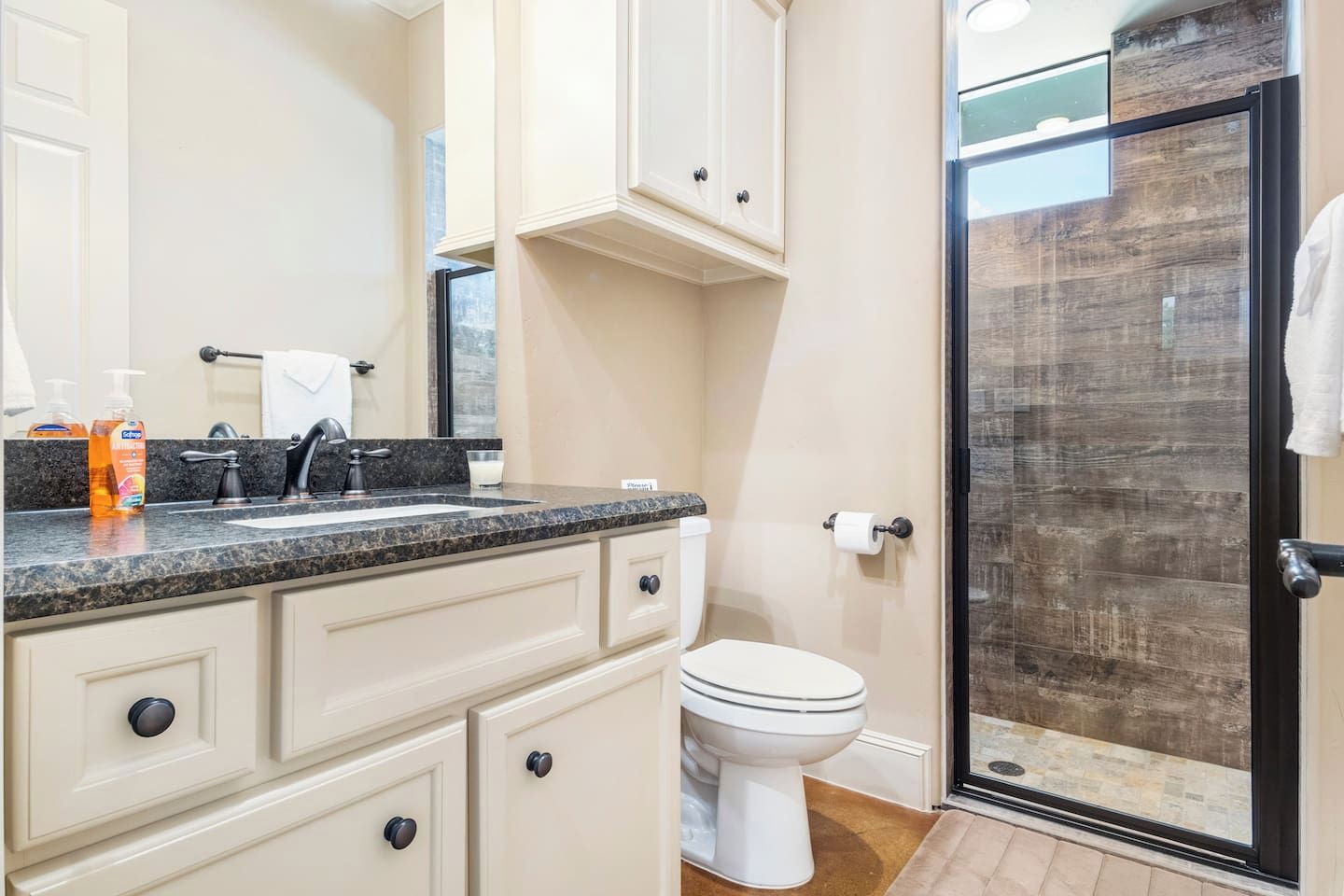 A bathroom with a granite countertop, a white toilet, and a glass shower enclosure.