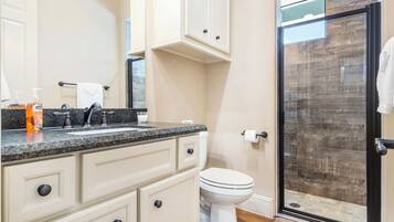 A bathroom with a granite countertop, a white toilet, and a glass shower enclosure.