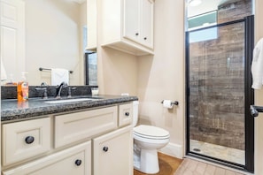 Une salle de bain dotée d’un comptoir en granit, de toilettes blanches et d’une cabine de douche en verre.