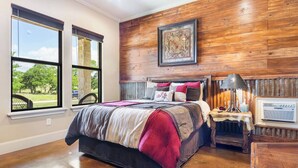 A bedroom with a large bed, a nightstand, a lamp, and a framed picture on the wall. - Timbuctoo 1 | Ranch Stay w/ Wildlife Views (Bandera)