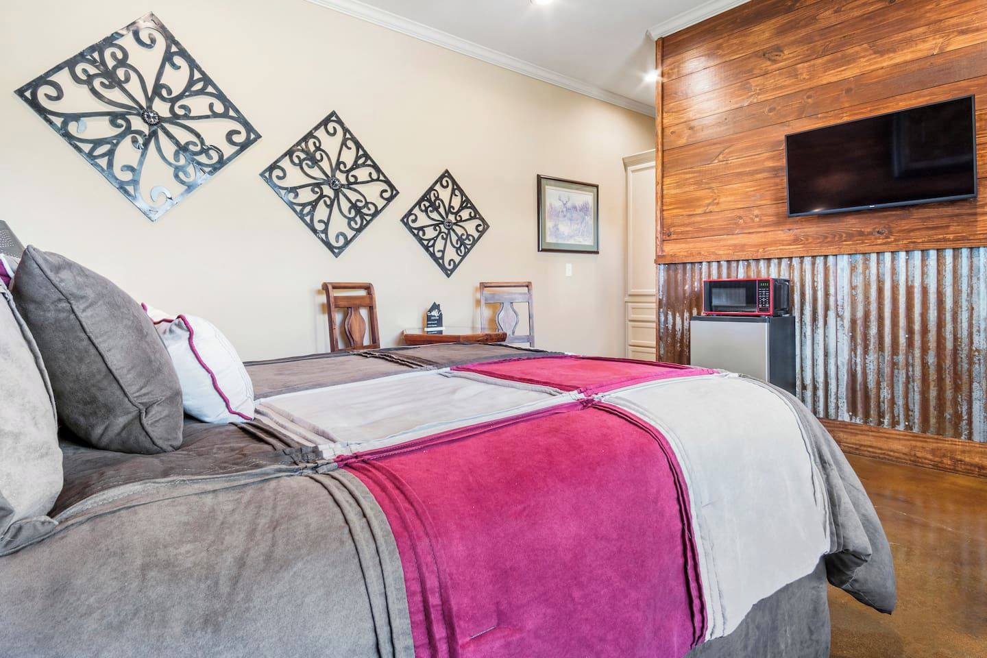 A bedroom with a bed, pillows, a flat-screen TV, a microwave, and decorative wall art.
