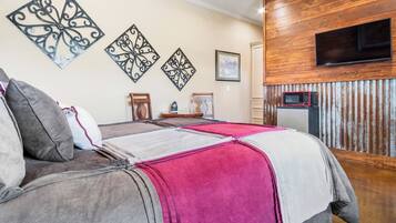 A bedroom with a bed, pillows, a flat-screen TV, a microwave, and decorative wall art.