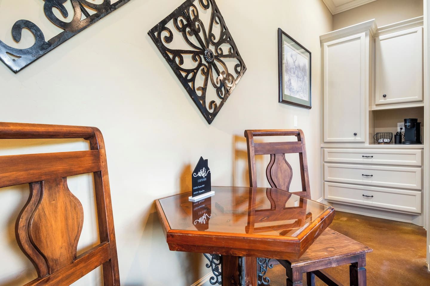 A dining area with a wooden table and chairs, a decorative wall piece, and a white cabinet with drawers.