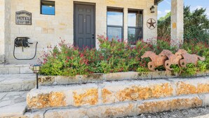 A stone building with a dark door, a sign indicating a hotel, and a decorative metal horse sculpture. - Timbuctoo 2 | Cozy Ranch Suite Near Cowboy Capital (Bandera)