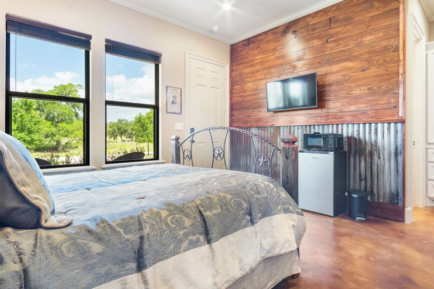 A bedroom with a bed, a TV mounted on a wooden wall, and a kitchenette area with a fridge and microwave.
