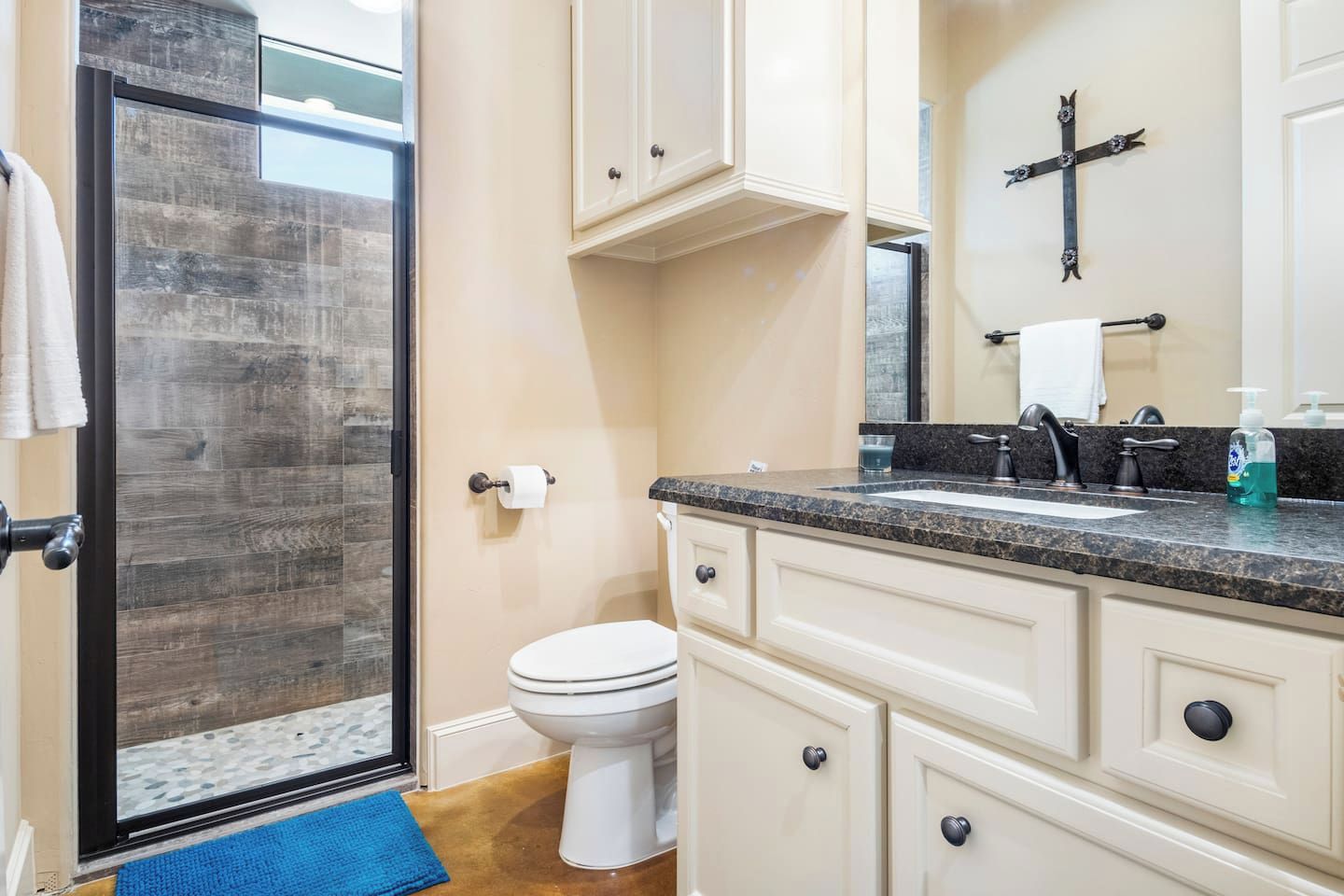 Une salle de bain avec une porte de douche en verre, des toilettes, un lavabo avec un robinet et des armoires.