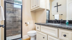 Een badkamer met een glazen douchedeur, een toilet, een wastafel met kraan en kastjes.