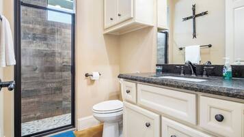 Une salle de bain avec une porte de douche en verre, des toilettes, un lavabo avec un robinet et des armoires.