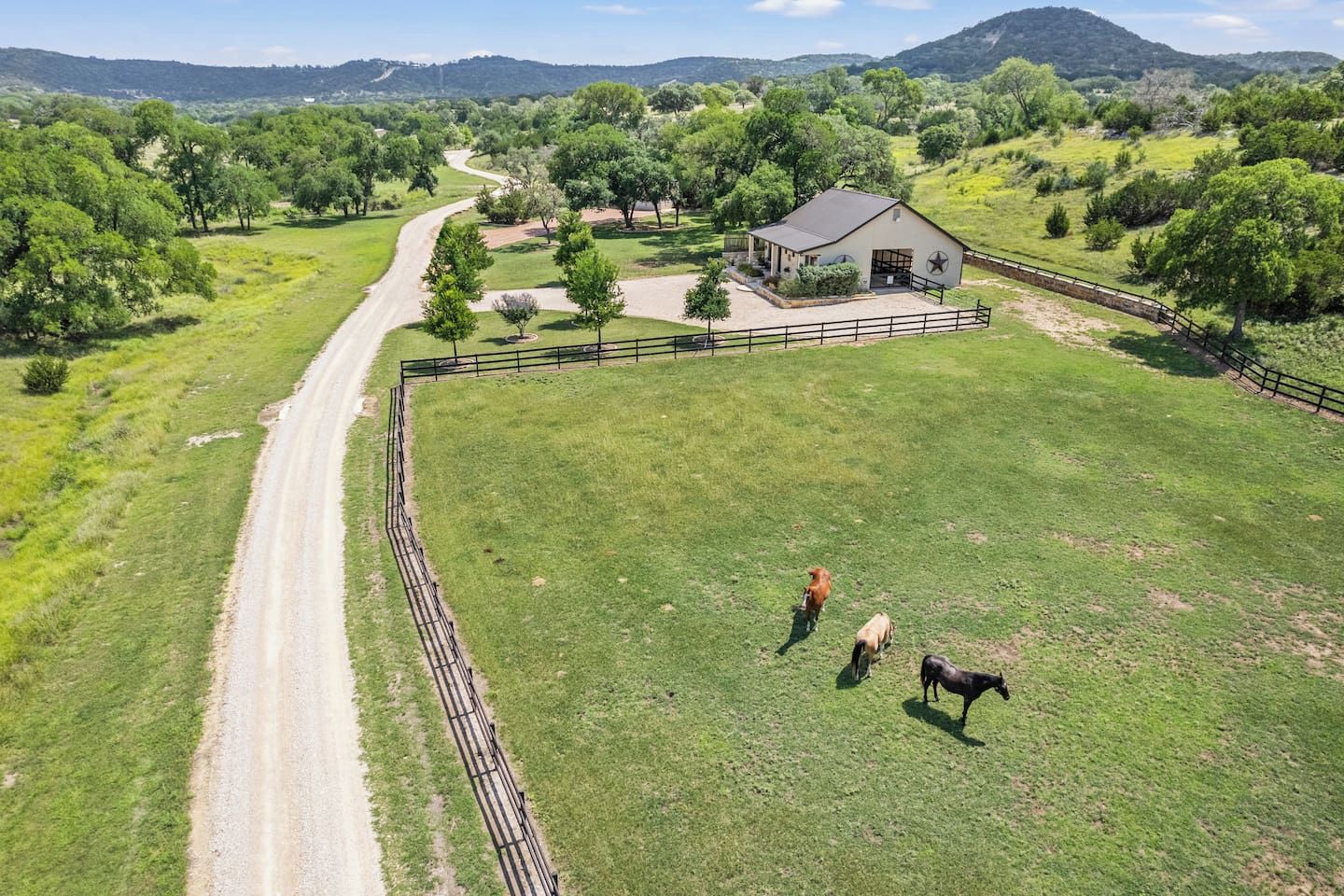 A fenced property with a dirt road, a barn, and a grassy field.