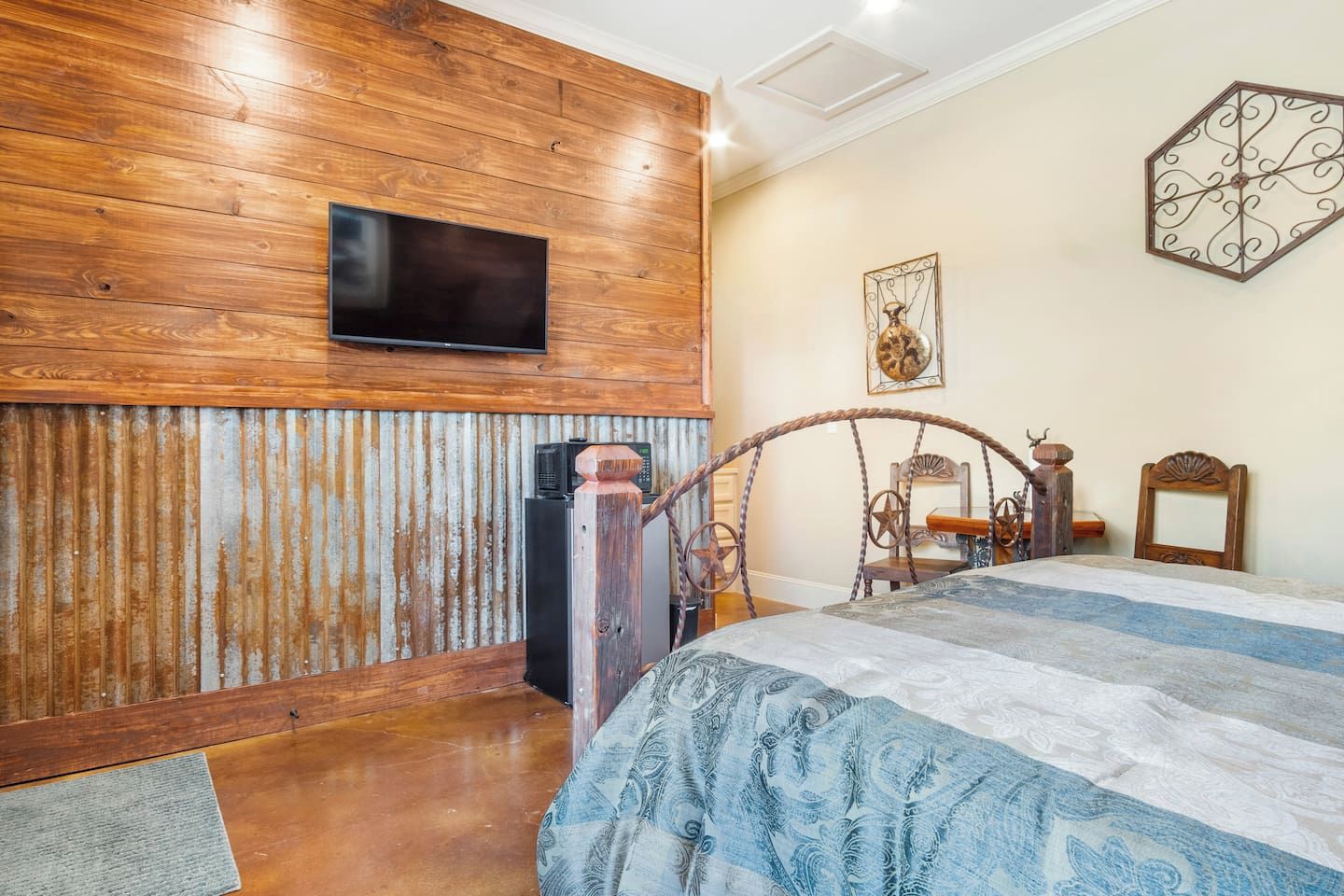 Une chambre avec un mur en bois, un lit recouvert d’une couvre-lit à motifs, un téléviseur fixé au-dessus du lit et un élément décoratif mural.