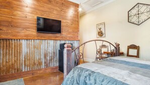 Een slaapkamer met een houten wand, een bed met een gebedrukte spreideken, een televisie boven het bed bevestigd, en een decoratief object aan de muur.