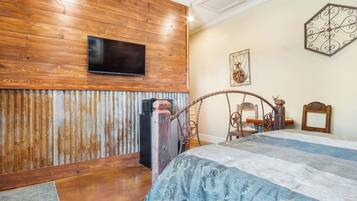 Une chambre avec un mur en bois, un lit recouvert d’une couvre-lit à motifs, un téléviseur fixé au-dessus du lit et un élément décoratif mural.