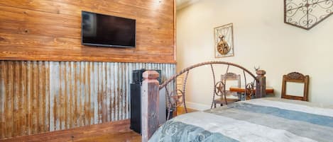 A bedroom with a wooden wall, a bed with a patterned bedspread, a television mounted above the bed, and a decorative wall piece.