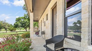 A covered outdoor seating area with wicker furniture and a stone building. - Timbuctoo 2 | Cozy Ranch Suite Near Cowboy Capital (Bandera)