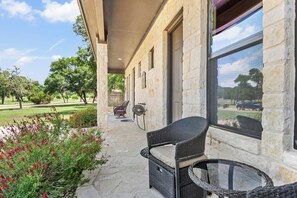 A covered outdoor seating area with wicker furniture and a stone building. - Timbuctoo 2 | Cozy Ranch Suite Near Cowboy Capital (Bandera)