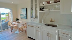 Een moderne keuken met witte kasten, een marmeren werkblad en uitzicht op het buitenleven door een schuifdeur.