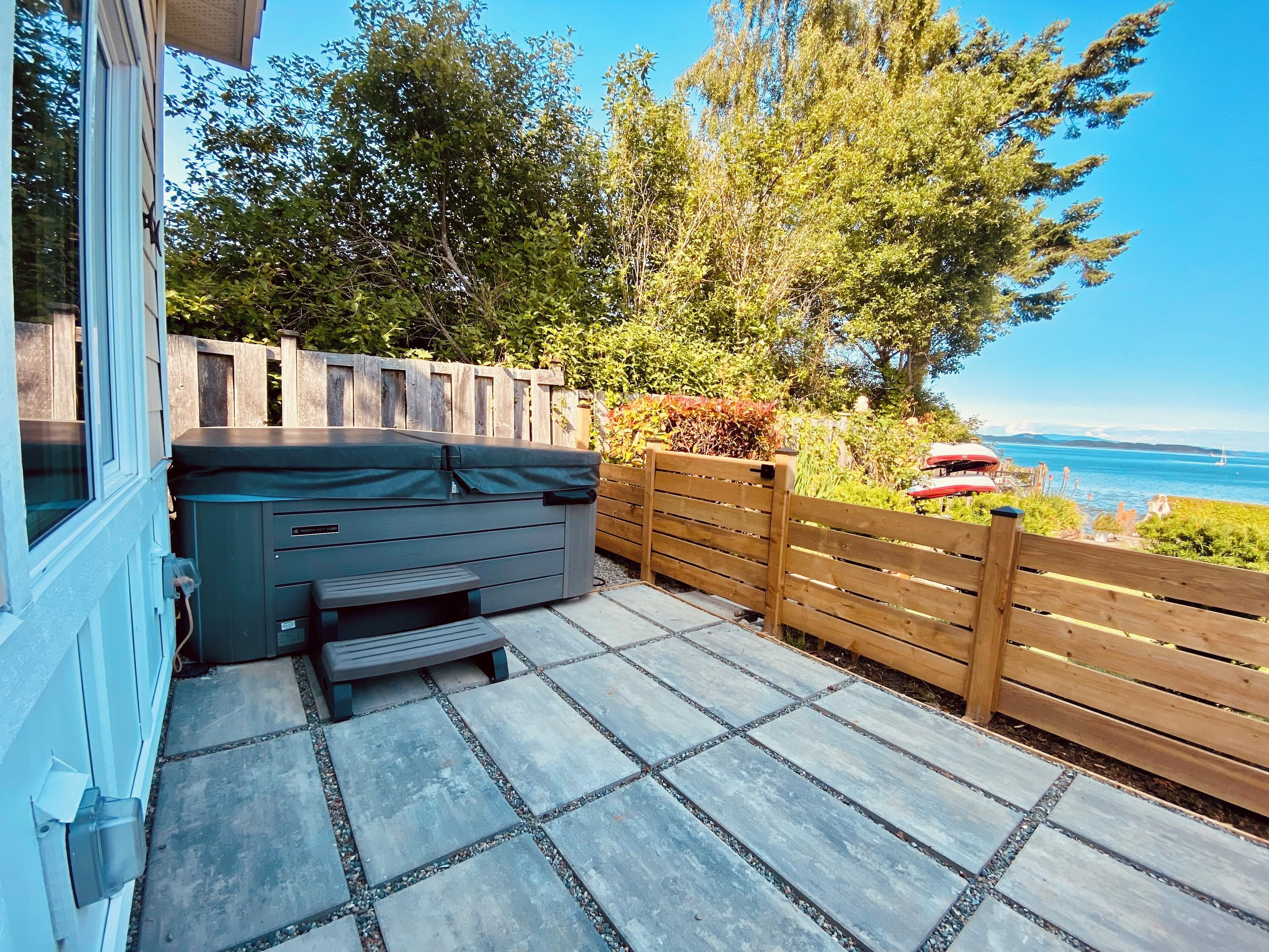 Une terrasse dotée d’un jacuzzi, de carreaux en pierre, d’une clôture en bois et offrant une vue sur la mer.
