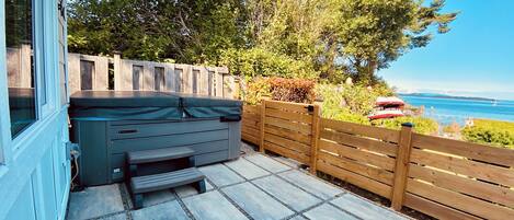 Une terrasse dotée d’un jacuzzi, de carreaux en pierre, d’une clôture en bois et offrant une vue sur la mer.