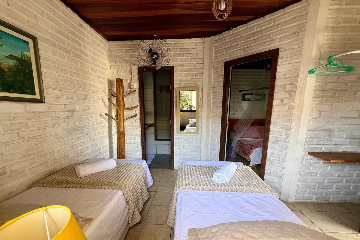 A room with two beds, a wooden ceiling, a white brick wall, and a yellow lamp.