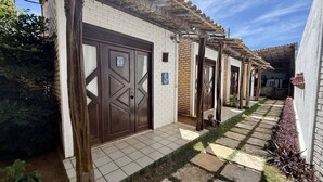 A row of traditional-style buildings with brick and white walls, wooden doors, and a tiled pathway. - Oceana Suites Villas de Tibau (Tibau do Sul)