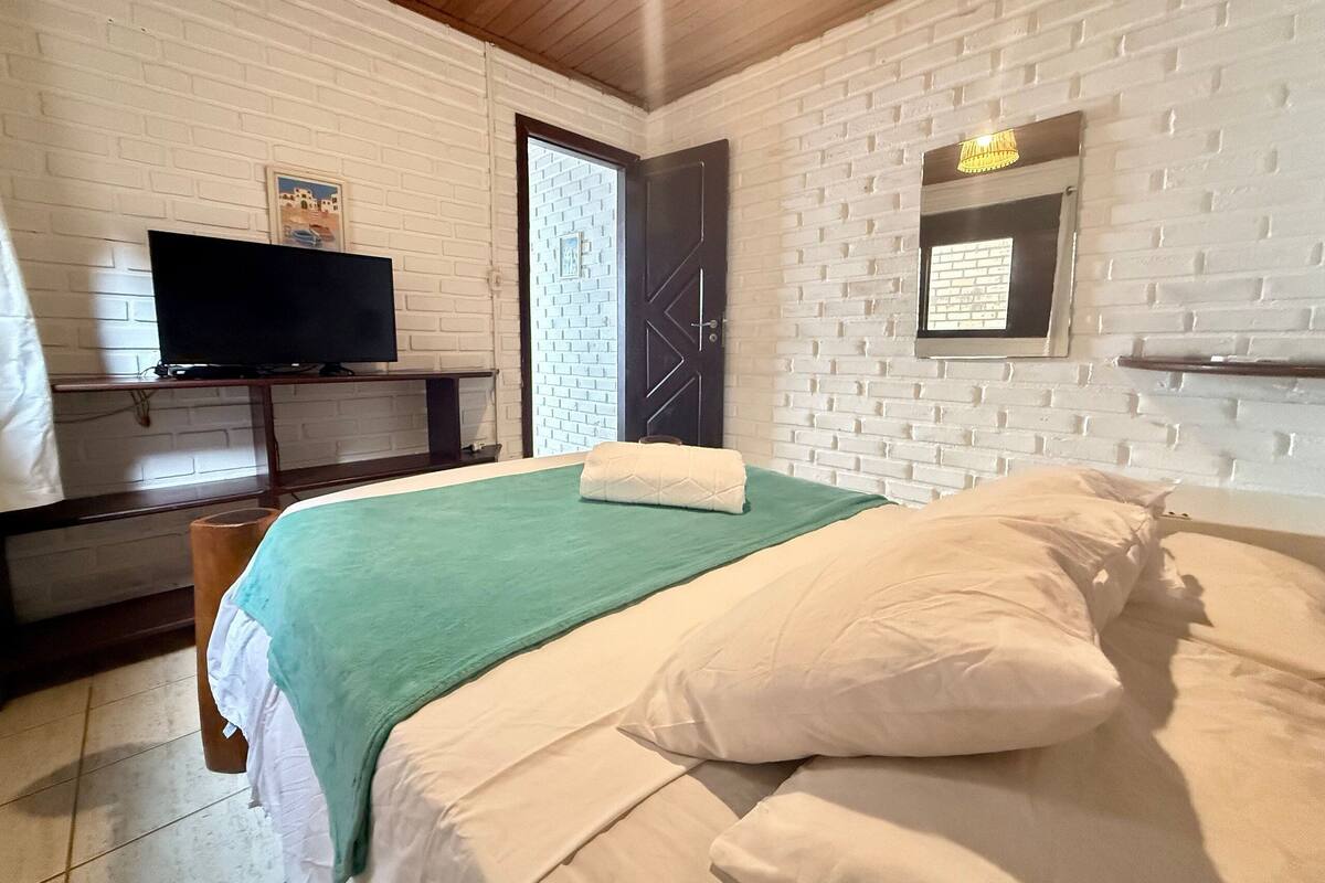 A bedroom with a bed, a television on a stand, a door, and a wall-mounted shelf.