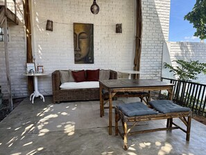 Un área de estar al aire libre acogedora con un sofá de mimbre, una mesa de madera y un banco acolchado.