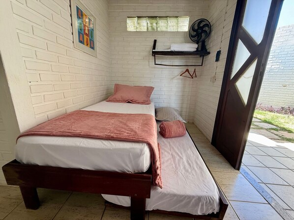 A small, well-lit room with a bed, a bench, a fan, and a window. - Oceana Suites Villas de Tibau (Tibau do Sul)
