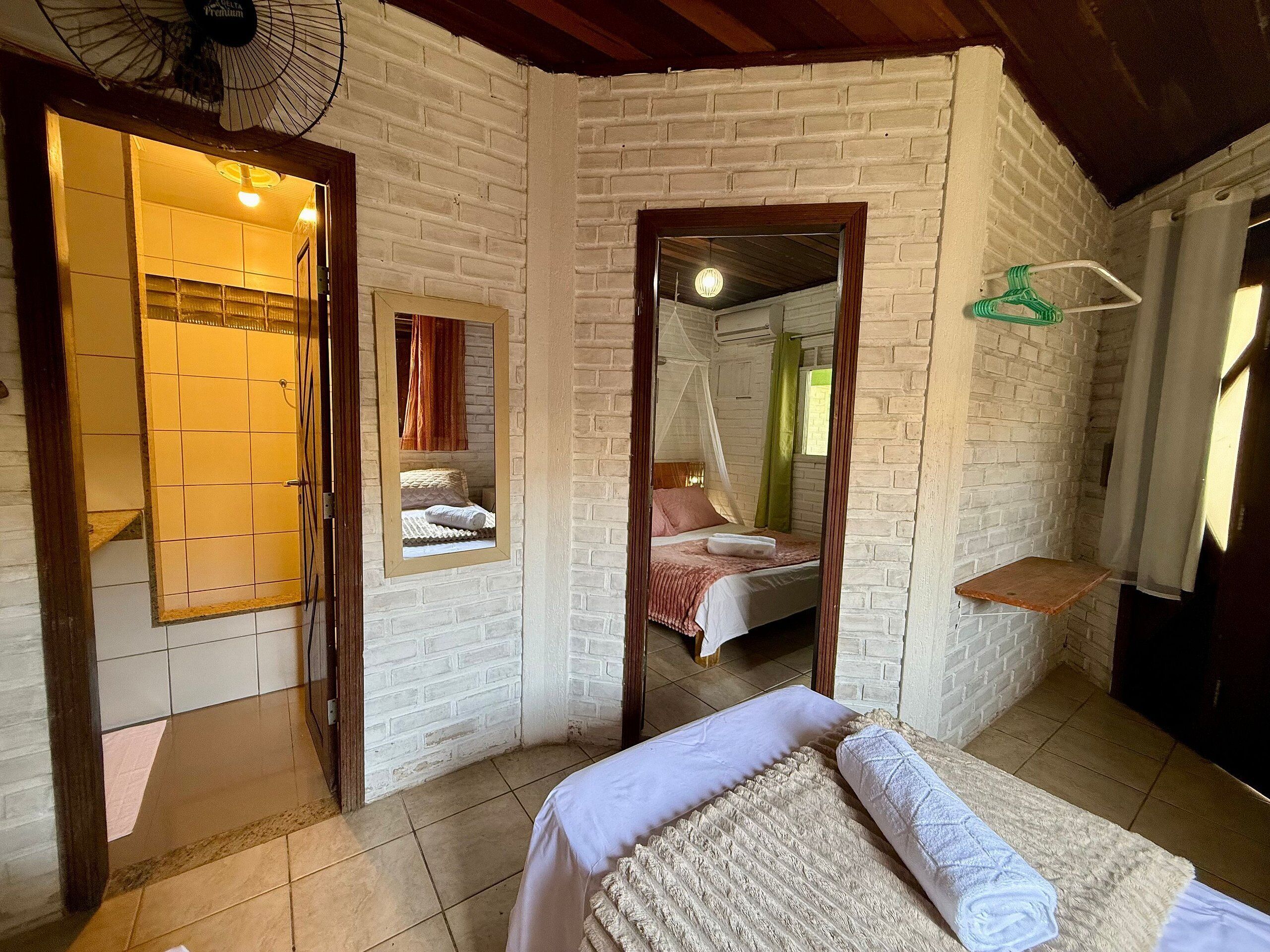 A bedroom with a bed, a mirror, a hanging light fixture, and a brick wall.