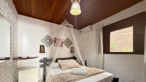 A bedroom with a bed, bedside table, air conditioning unit, and a window with a view of greenery. - Oceana Suites Villas de Tibau (Tibau do Sul)