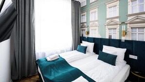 A hotel room with a large bed, grey curtains, a teal bedspread, and a classic architectural wall design. - Wiślna Main Square Apartments Self Check-in (Kraków)