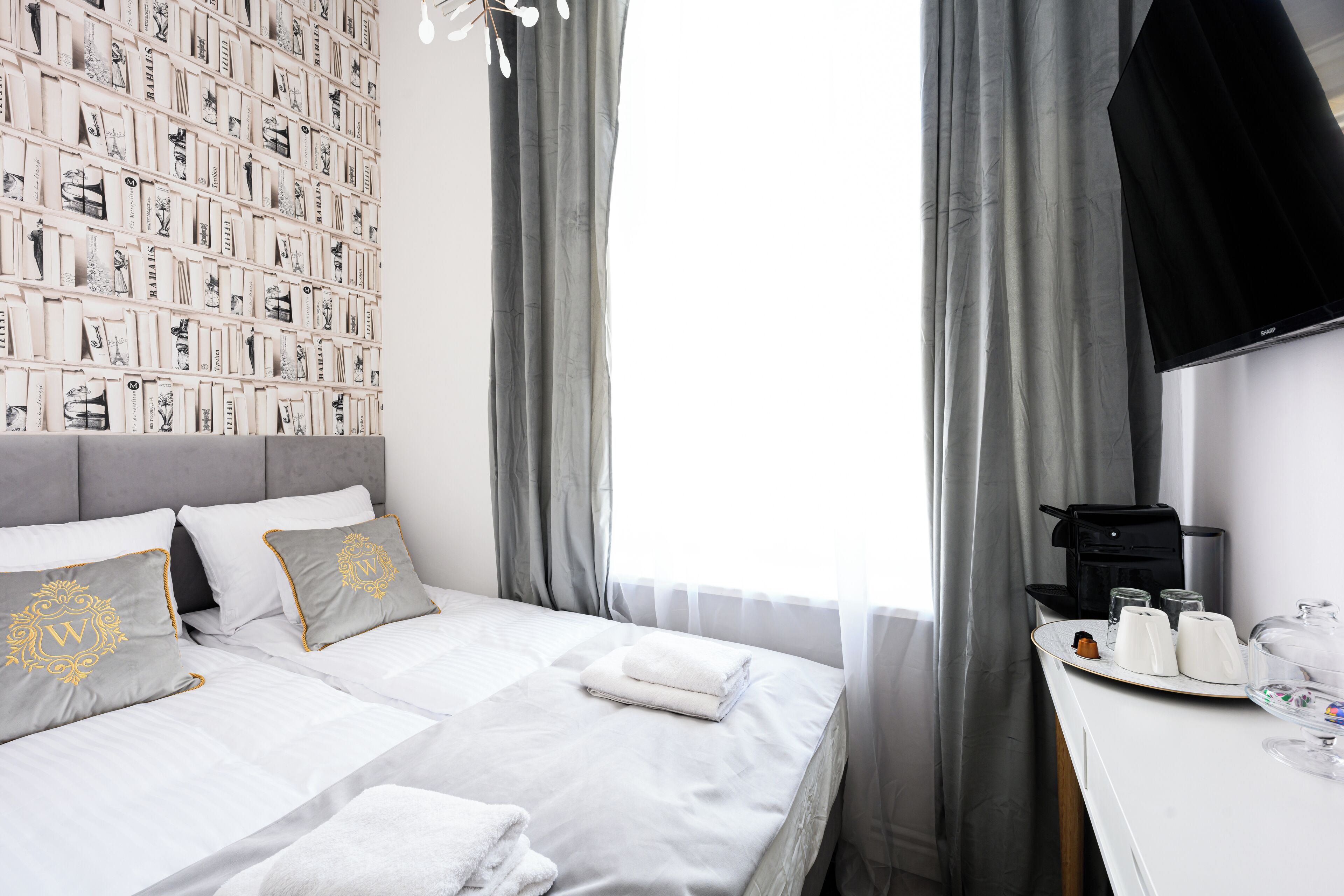 A hotel room with a neatly made bed, a wall-mounted TV, and a breakfast tray with coffee and tea.