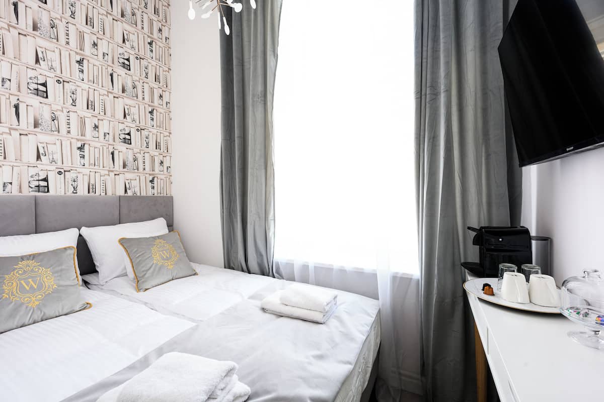A hotel room with a neatly made bed, a wall-mounted TV, and a breakfast tray with coffee and tea.