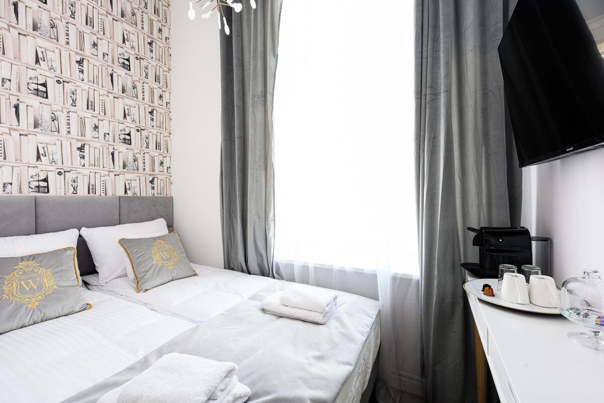 A hotel room with a neatly made bed, a wall-mounted TV, and a breakfast tray with coffee and tea.