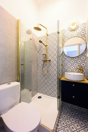 Ein Badezimmer mit Toilette, einer Duschkabine, einem Waschbecken mit Goldarmatur und einem Fliesenboden mit Muster.